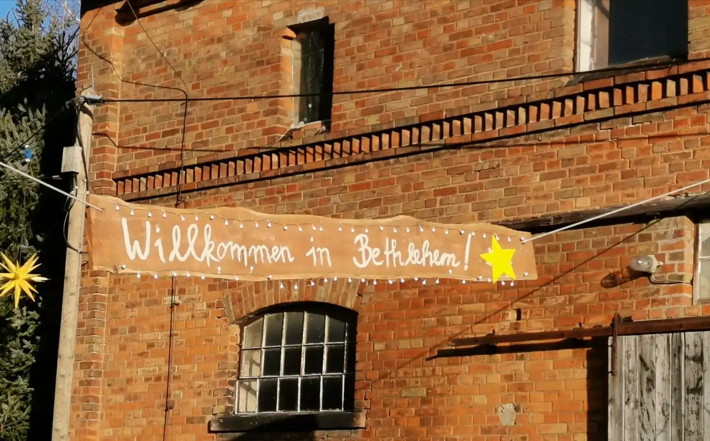 Backsteinfassade mit einem Holzbanner und Lichterkette: „Willkommen in Bethlehem!“, daneben ein gelber Stern.